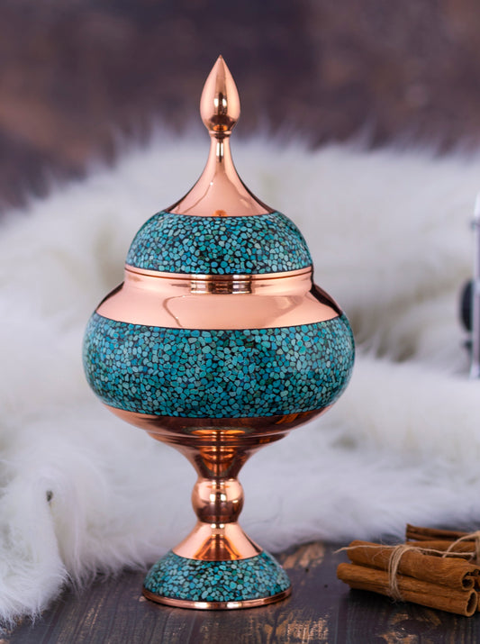 Decorative teal and copper urn on a wooden surface with a vintage camera in the background.
